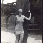 Real Photo Miss Train stands in front of a surfboard in front of the Outrigger Canoe Club, 1915