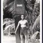Real Photo Duke stands in font of his surfboard at Waikiki Beach, used in 1931